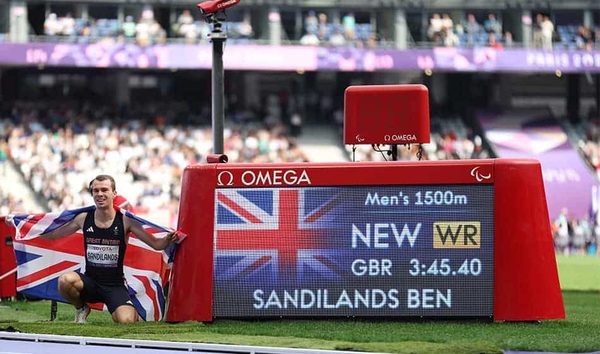 A athlete kneels beside a stadium scoreboard showing Men's 1500m, New WR, GBR 3:45.40 and Sandilands Ben, with a Union flag.