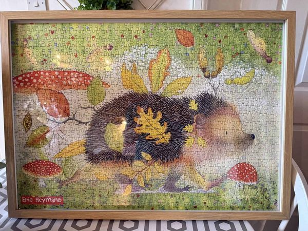Framed hedgehog jigsaw puzzle showing a hedgehog with autumn leaves on its back, among red toadstools and fallen leaves.