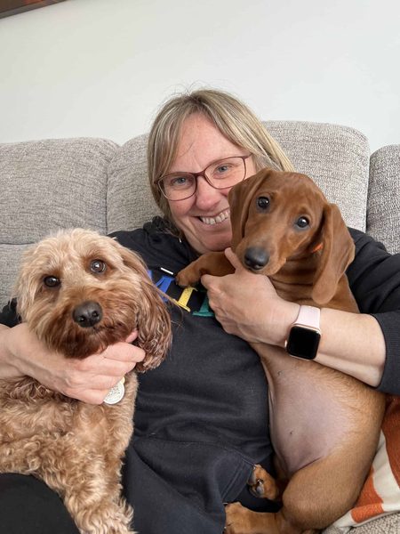 Sharon smiles on a sofa holding a fluffy apricot dog and a brown dachshund.