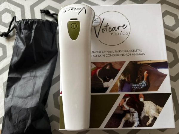 White handheld Vetcare Photizo device lying on its boxed packaging beside a black drawstring bag.