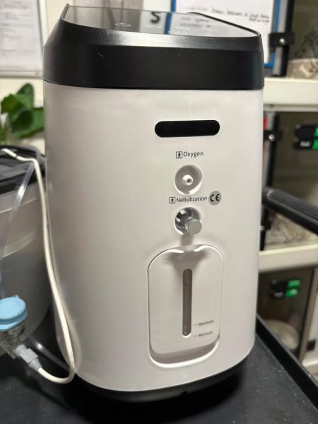 White and black oxygen and nebulisation machine with a tube running from it to a blue-capped connector.