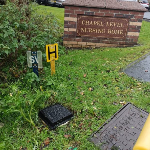 Black cover and hydrant marker in grass beside a brick sign reading Chapel Level Nursing Home.